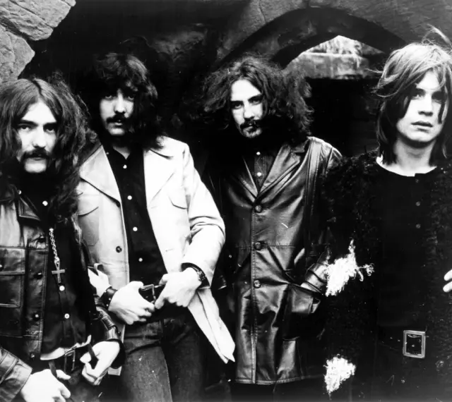 Członkowie zespołu Black Sabbath pozują do zdjęcia w mrocznym otoczeniu.
