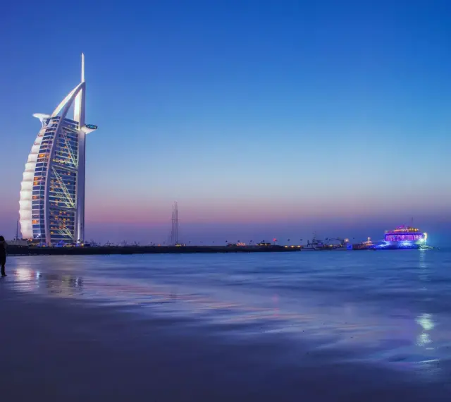 Zachód słońca nad Zatoką Perską. Widok na hotel Burj Al Arab i oświetloną łódź. Ceny w Dubaju mogą być wysokie, ale widoki są bezcenne.