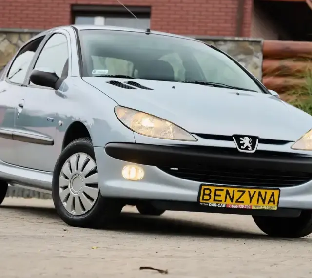 Jasny Peugeot 206 1.4 benzyna z żółtą tablicą "BENZYNA" na zderzaku, zaparkowany na zewnątrz.