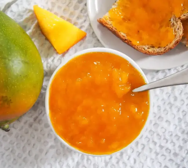 Słoik z dżemem z mango, obok świeży owoc i kromki chleba. Codzienne jedzenie mango to pyszny początek dnia.
