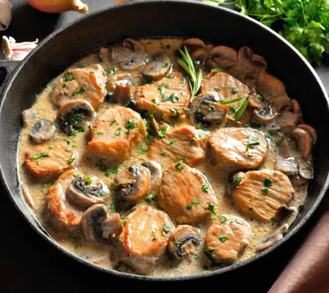 Soczysty schab w sosie pieczarkowym, udekorowany natką pietruszki, podany w żeliwnej patelni. Aromatyczne danie, które zachwyca smakiem.