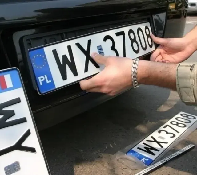 Montaż nowych tablic rejestracyjnych. Jedna z nich, z numerem WX 37808, jest właśnie wkładana. Obok leży kolejna, jeszcze w folii.