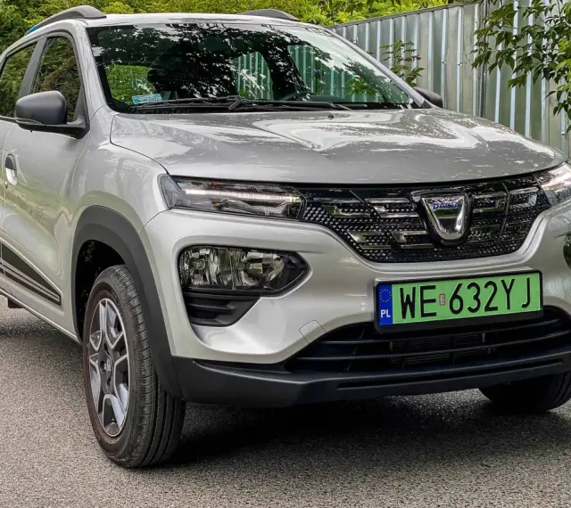 Srebrna Dacia Spring z zieloną tablicą rejestracyjną WE 632YJ, przód samochodu.