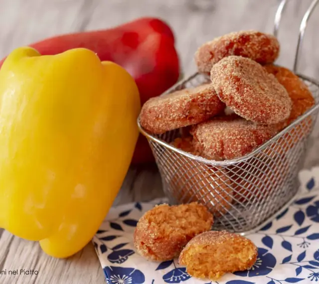 Polpette di peperoni dorate e croccanti, servite in un cestino, accanto a peperoni freschi rossi e gialli.