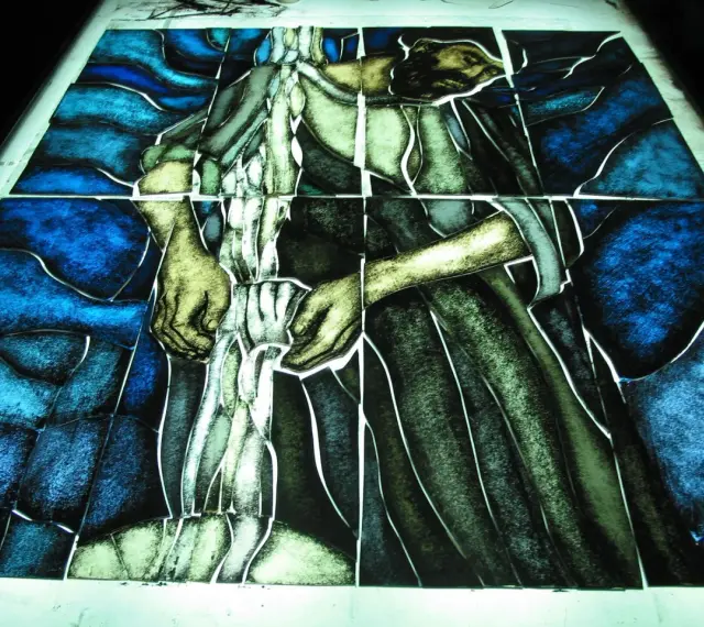 Fragment witrażu w stylu modernizm, przedstawiający postać w niebieskim i zielonym tle.