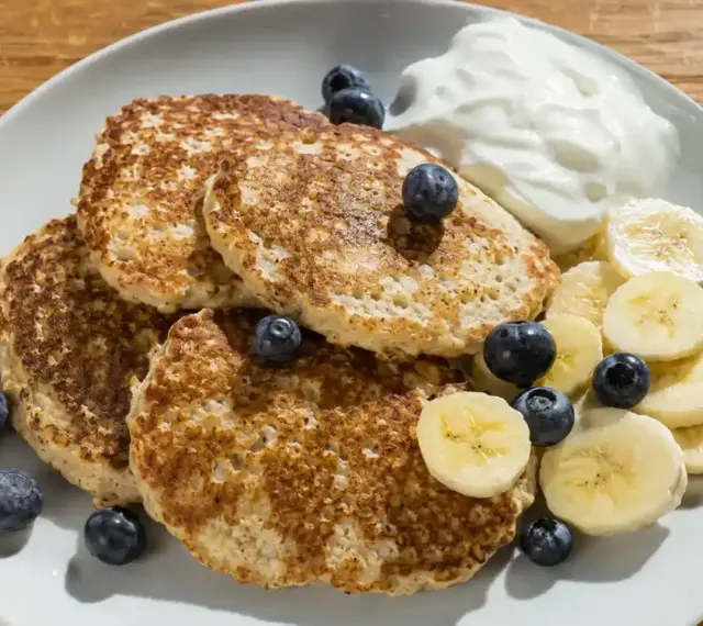 En tallrik med bananpannkakor, blåbär, bananskivor och en klick yoghurt. Ett enkelt bananpannkaka recept för en god frukost.