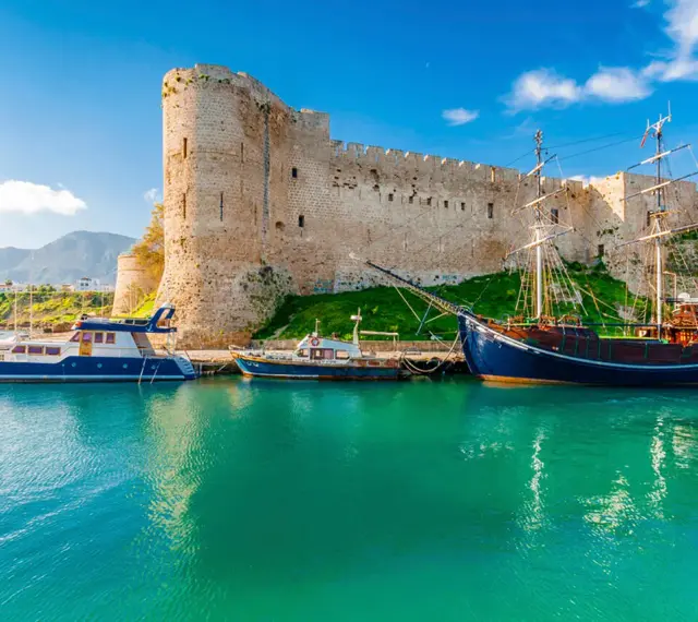 Zamek Kyrenia na Cyprze Północnym z łodziami przycumowanymi w turkusowej zatoce.