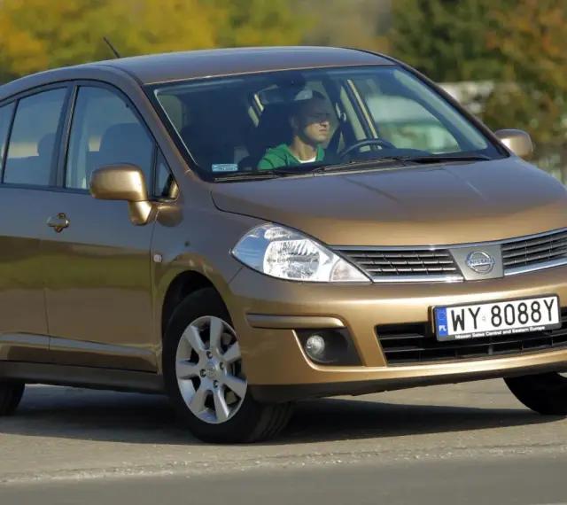 Złoty Nissan Tiida z mężczyzną za kierownicą jedzie po drodze.