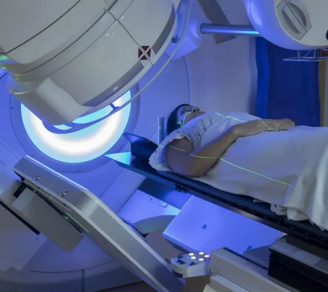 Pacjentka leży na stole zabiegowym pod aparatem do radioterapii, na jej ciele widoczne są zielone linie naprowadzające.