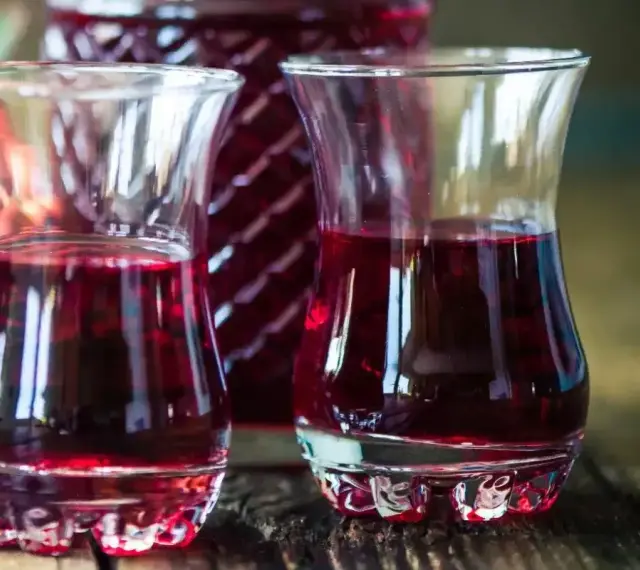Dwa kieliszki wypełnione rubinową nalewką z czeremchy, obok butelka i kiść owoców.