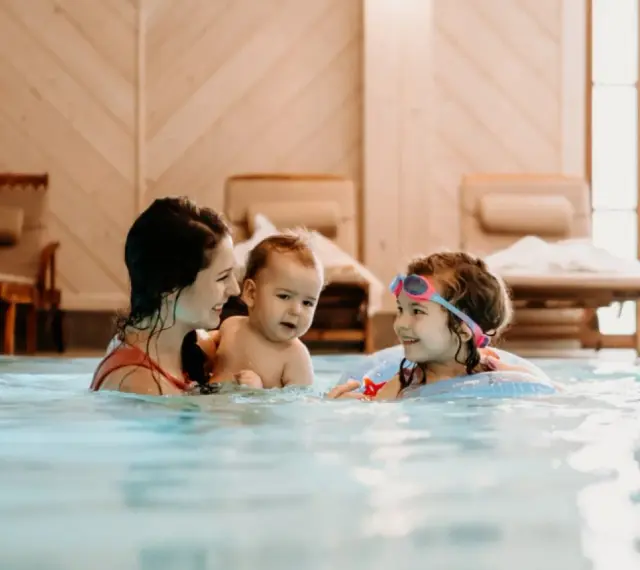 Rodzina cieszy się basenem w hotelu dla dzieci w Wiśle. Mama z dwójką dzieci pluska się w wodzie, tworząc radosne wspomnienia.