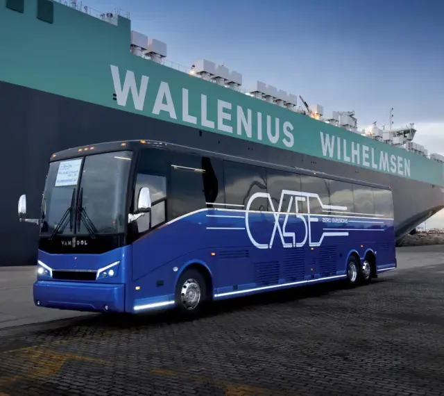 Niebieski autokar Van Hool CX45 z napisem "ZERO EMISSIONS" stoi przy ogromnym statku Wallenius Wilhelmsen.