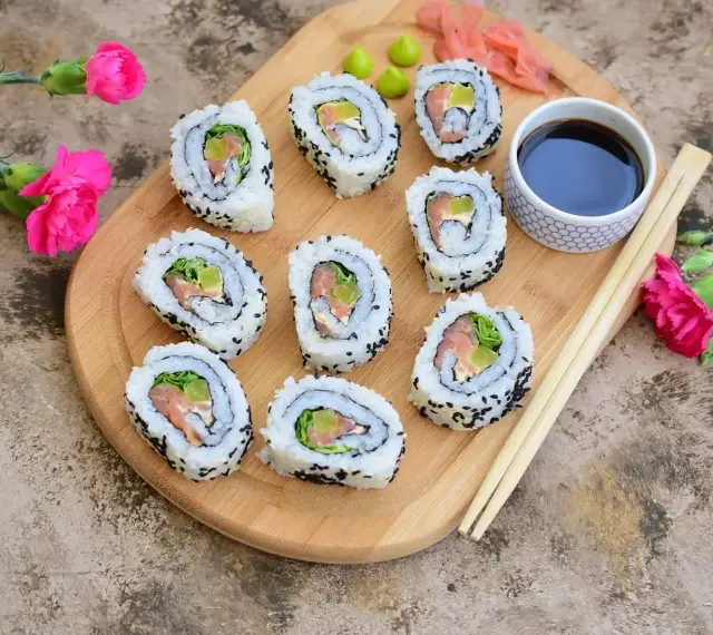 Pyszne california sushi z łososiem i awokado, posypane czarnym sezamem, podane z sosem sojowym i wasabi.