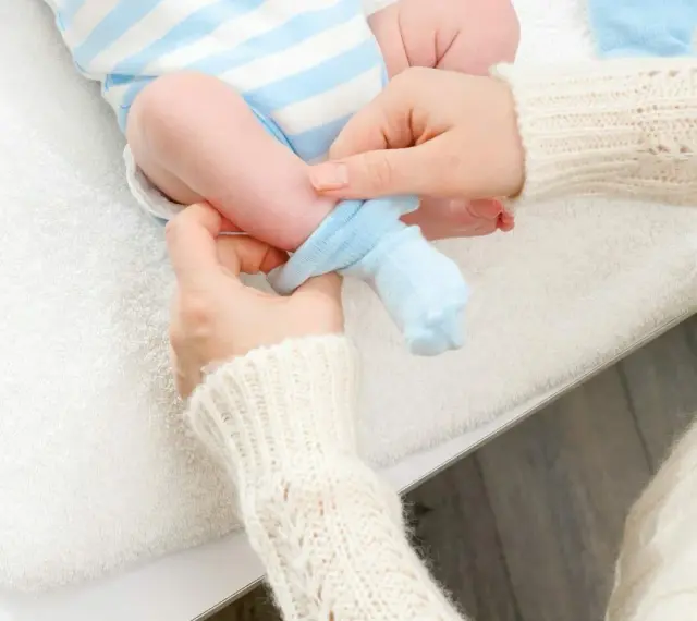 Mama zakłada niebieskie skarpetki na nóżki noworodka. Dobieranie odpowiedni jaki rozmiar skarpetek dla noworodka jest ważne.