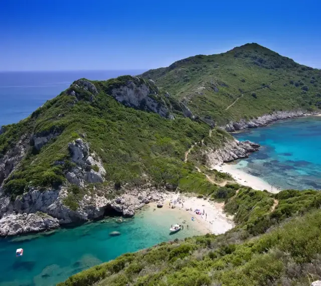 Malownicza zatoka z turkusową wodą i piaszczystą plażą, otoczona zielonymi wzgórzami. Tak właśnie wygląda Korfu, grecka wyspa, gdzie leży ten raj.