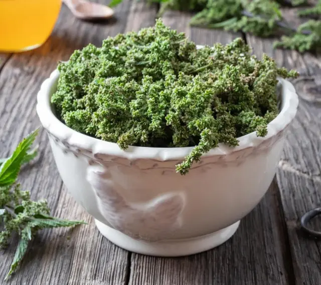 Schale mit Brennesselsamen, die ihre positive brennesselsamen wirkung für die Gesundheit andeuten. Daneben ein Glas mit gelber Flüssigkeit.