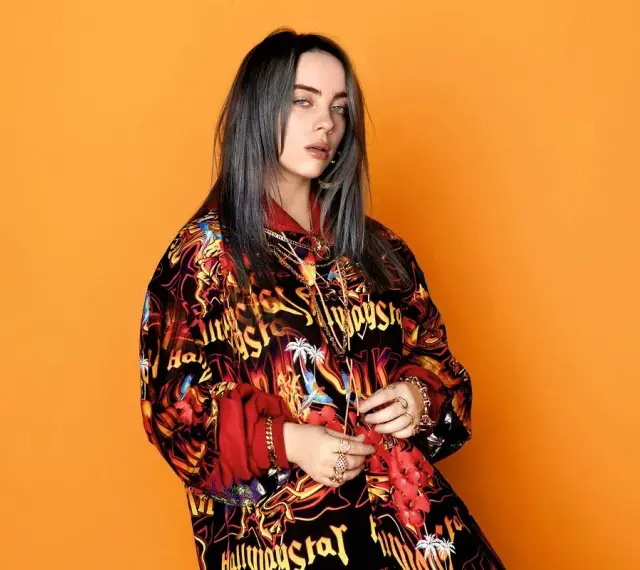Billie Eilish w kolorowej bluzie, z mnóstwem złotych łańcuchów i pierścionków, jakby przygotowywała się do odebrania kolejnych nagród.