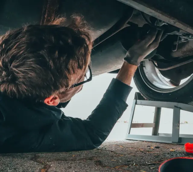 Mężczyzna naprawia podwozie Opla p1700. Widać jego rękę w rękawicy, narzędzia i puszkę WD-40.