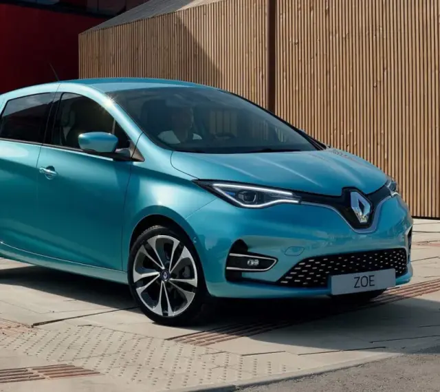 Błękitny Renault Zoe z nowoczesnymi światłami LED stoi na tle drewnianej elewacji.