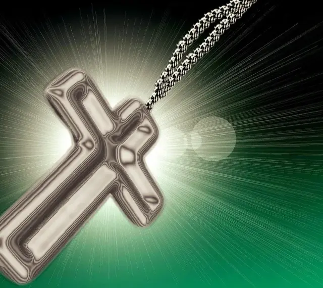 Metalowy krzyż na sznurku, otoczony blaskiem. Symbolizuje nadzieję i nawrócenie, światło rozchodzące się na zielonym tle.