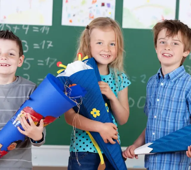 Drei Kinder mit Schultüten vor einer Tafel. Die Einschulung in Sachsen-Anhalt 2025 wird hier fröhlich gefeiert.