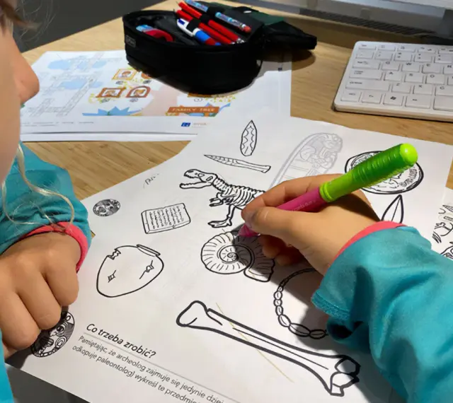Dziecko koloruje edukacyjne karty pracy z dinozaurem i artefaktami.
