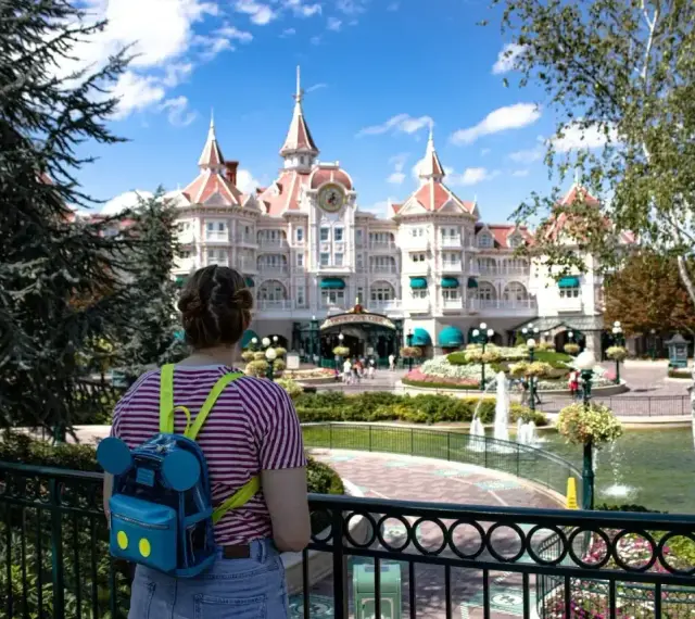 Dziewczyna z plecakiem w kształcie Myszki Miki podziwia zamek w Disneyland Paris. Bilety do parku już kupione, czas na przygodę!