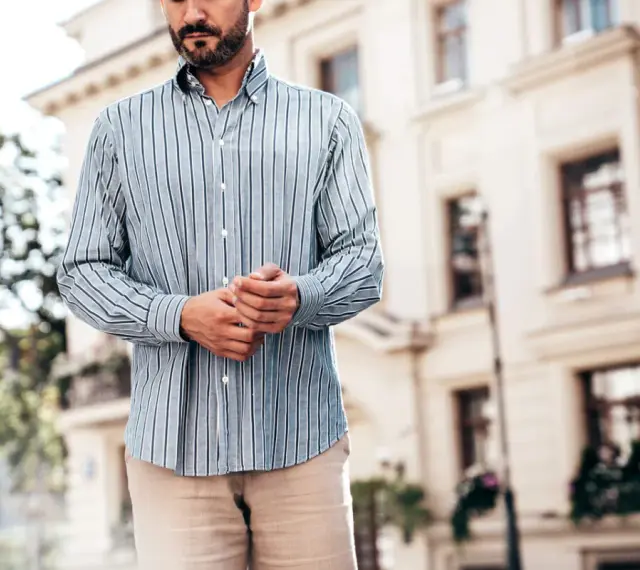 Mężczyzna w paski koszuli, z rękami złożonymi na brzuchu, idealnie pokazuje, kiedy koszula w spodnie tworzy elegancki look.