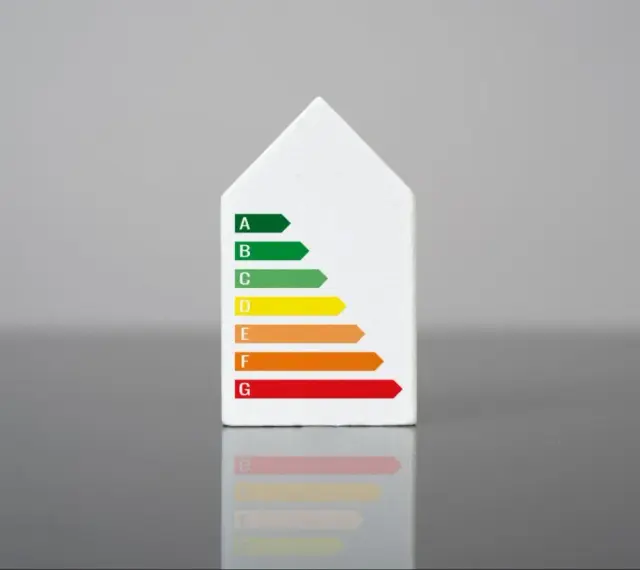 Biały model domu z naklejką klasy energetycznej. Świadectwo energetyczne mieszkania ocenia jego efektywność.