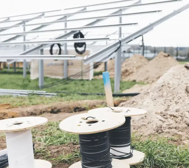 Na placu budowy paneli słonecznych przygotowywane są kable do uziemienia. Widać szpule z przewodami i metalowe konstrukcje.