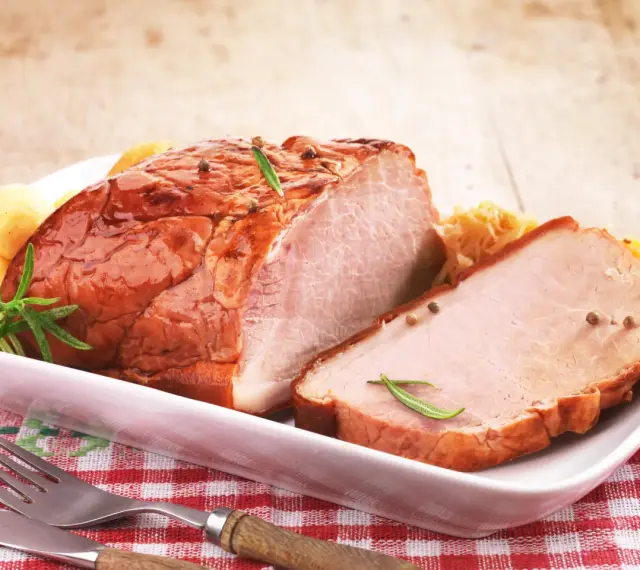 Pyszny, pieczony schab na wielkanoc, udekorowany rozmarynem i ziarnami pieprzu, podany z ziemniaczkami i surówką.