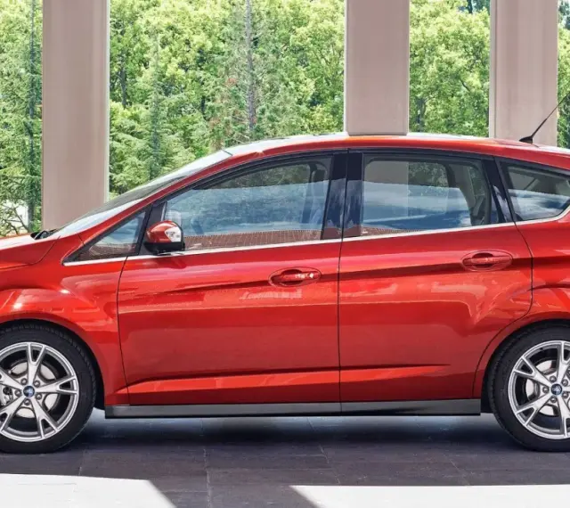 Czerwony Ford C-Max 1.6 benzyna zaparkowany pod arkadami, z zielenią w tle.