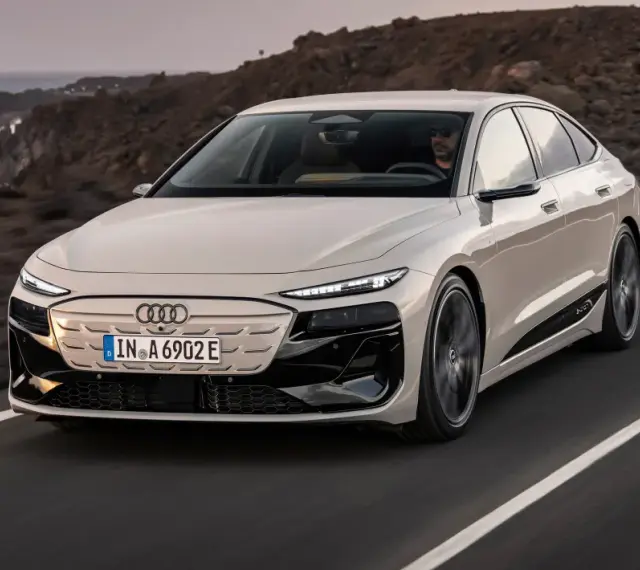 Jasnoszary Audi A6 e-tron jedzie po drodze z widokiem na ocean i góry.