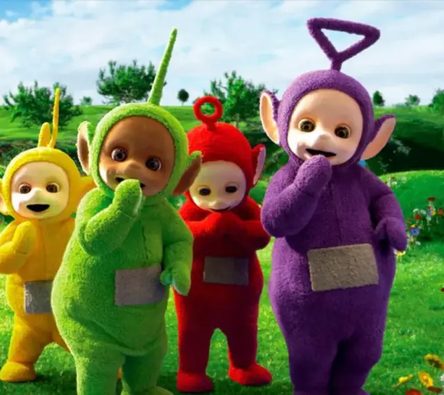 Teletubisie imiona: Tinky Winky, Dipsy, Laa-Laa i Po stoją na zielonej łące pełnej kwiatów.