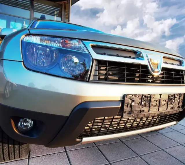 Złoty Dacia Duster 1.6 benzyna z chromowanym grillem i niebieskimi reflektorami, gotowy na przygodę pod błękitnym niebem.
