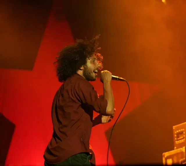 Zac Zack de la Rocha śpiewa z pasją na koncercie Rage Against the Machine. Czerwona gwiazda w tle podkreśla energię występu.