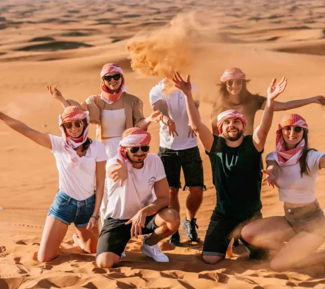 Grupa przyjaciół w tradycyjnych arabskich chustach bawi się piaskiem na pustyni. Wspaniałe wspomnienia z Dubaju w styczniu.