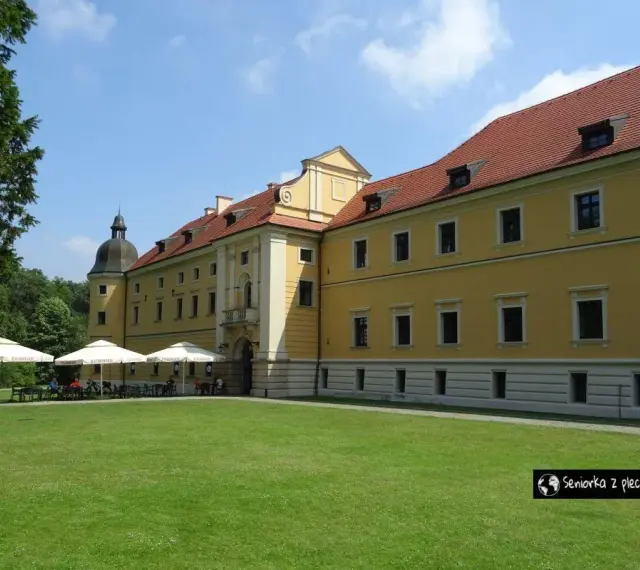 Żółty budynek opactwa cystersów w Rudach z czerwonym dachem i zielonym trawnikiem przed nim.