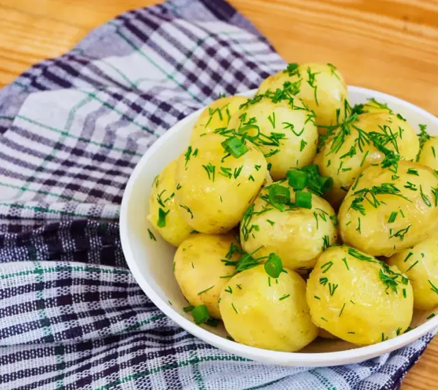 Młode ziemniaki w misce, posypane koperkiem i szczypiorkiem. Idealne na lato, a ile gotować młode ziemniaki? Krótko!