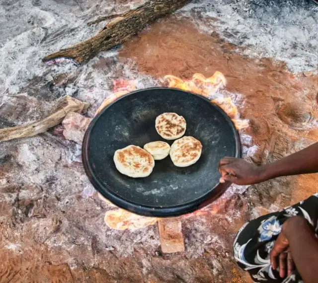 Kobieta przygotowuje afrykańskie jedzenie - placki smażone na ogniu na dużej patelni.