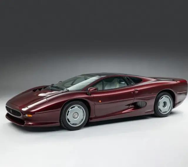 Bordowy Jaguar XJ220, ikona motoryzacji lat 90., prezentuje swoje aerodynamiczne linie na tle szarego tła.