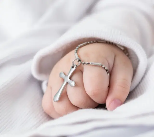 Dziecięca dłoń z krzyżykiem na bransoletce, symbol błogosławieństwa podczas chrzcin dziecka.