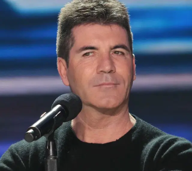 Simon Cowell, znany z surowych ocen, siedzi przy mikrofonie. Plotki o tym, że Simon Cowell nie żyje, są fałszywe.