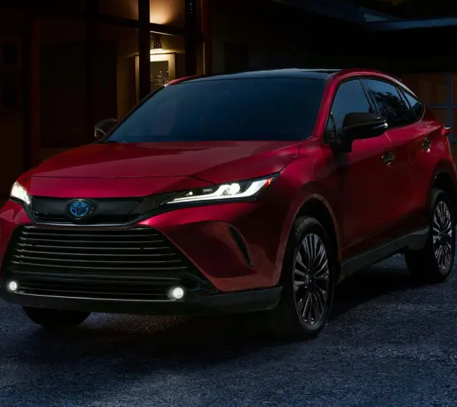 Elegancka, czerwona Toyota Venza z nowoczesnymi światłami LED stoi przed domem o zmierzchu.