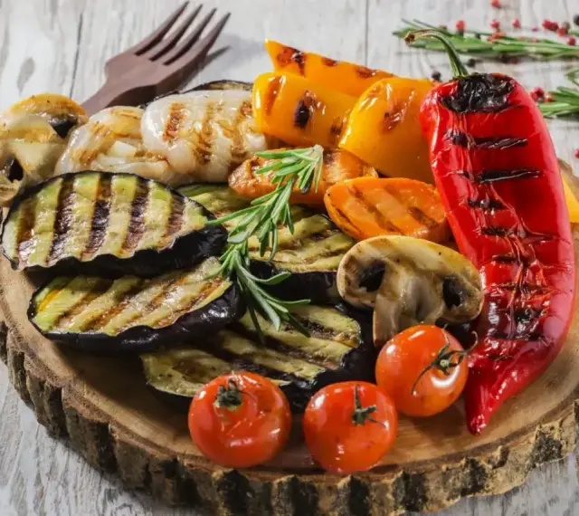 Grillowane warzywa: bakłażan, papryka, pieczarki, pomidorki i marchewka. Idealne dodatki do grilla, podane na drewnianej desce.