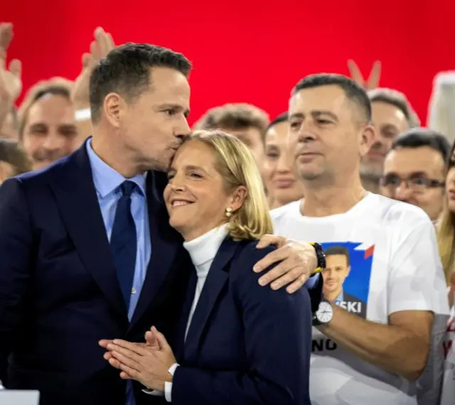 Rafał Trzaskowski, choć nie znamy jego dokładnego wieku, czule całuje żonę na tle tłumu.