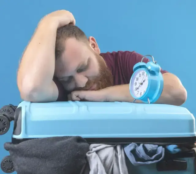 Zmęczony podróżnik śpi na walizce obok budzika. Czy to jetlag?