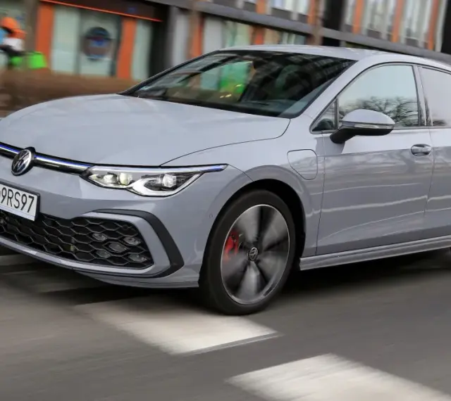 Szary Volkswagen Golf GTE porusza się po miejskiej drodze, z rozmytym tłem budynków i przechodniów.