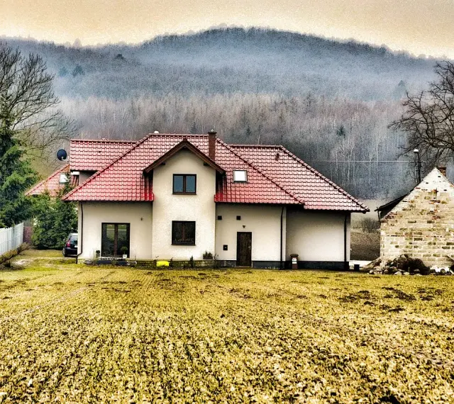 Dom z czerwonym dachem i polem przed nim. Rodzinna historia o przepisaniu domu na jedno dziecko bez zgody drugiego.