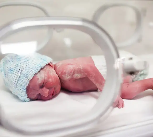 Maleńki noworodek w niebieskiej czapeczce leży w inkubatorze. To dziecko urodzone w 20 tygodniu ciąży, walczące o życie.